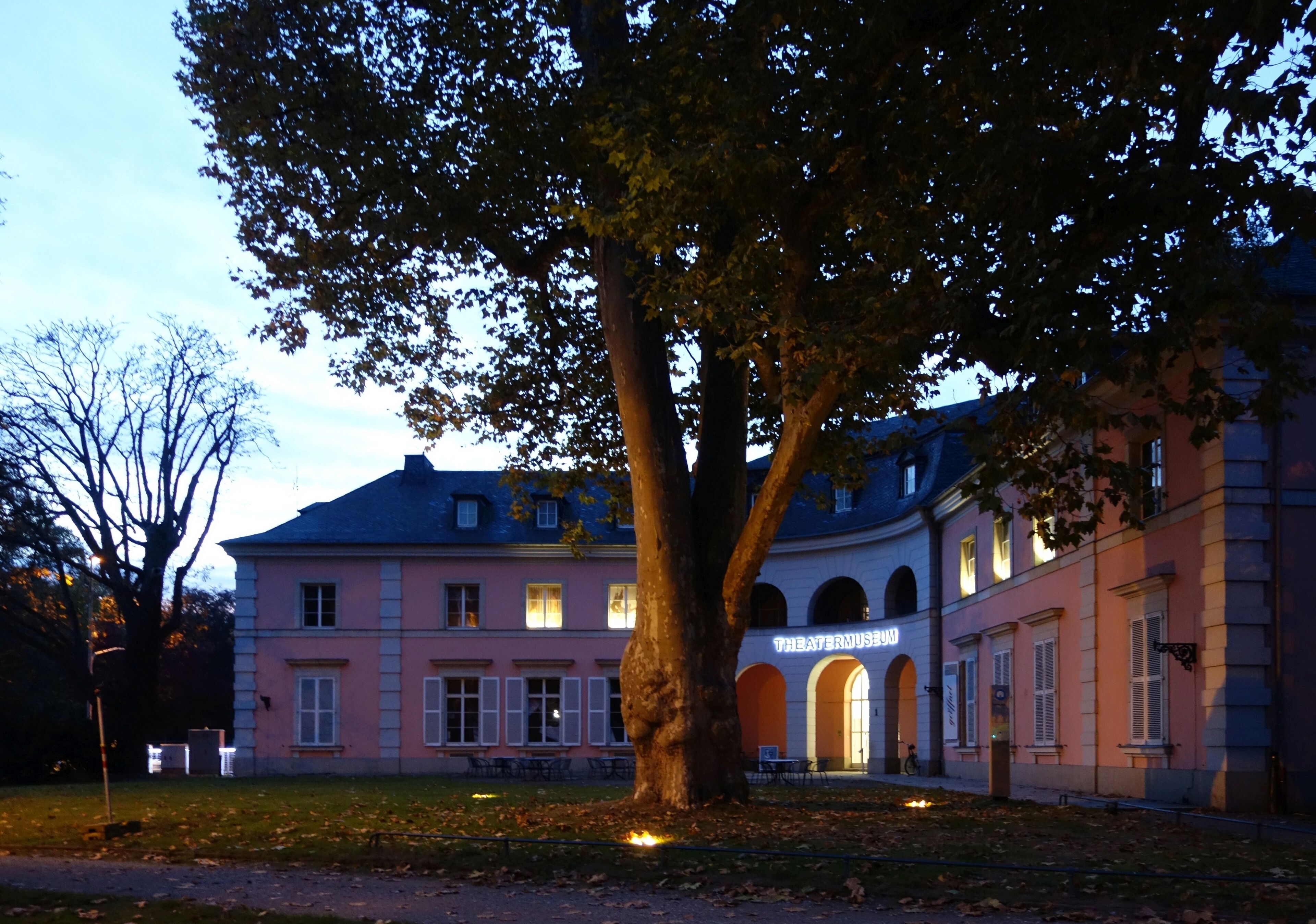 A pink building with a sign that reads "Theater Museum" and a large tree in front.