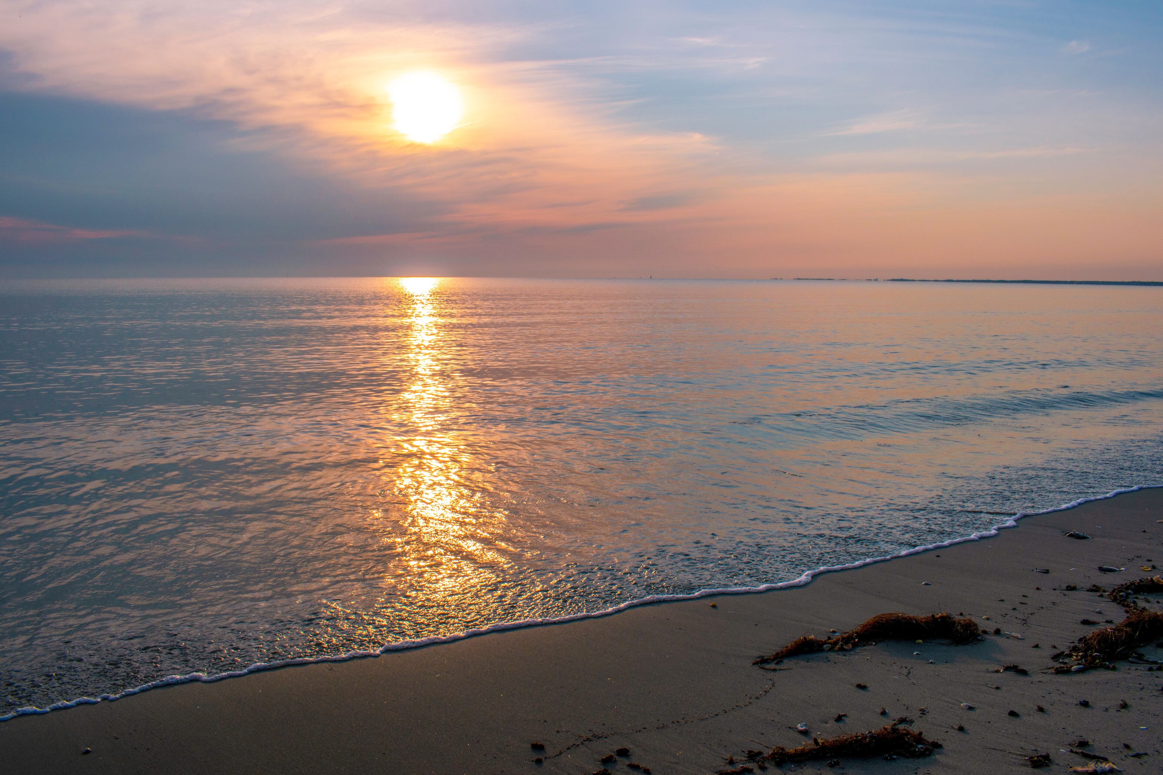 A sunset over a calm sea with a sandy beach.