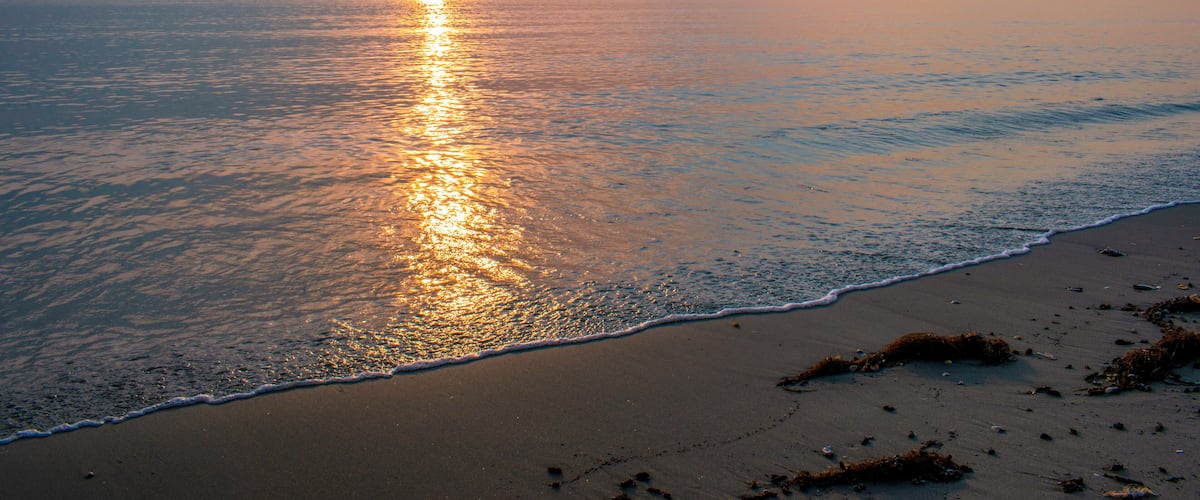 A sunset over a calm sea with a sandy beach.