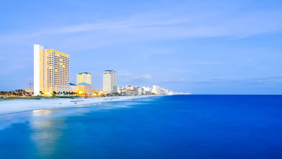 A coastal cityscape with a beach, high-rise buildings, and a clear blue sky.