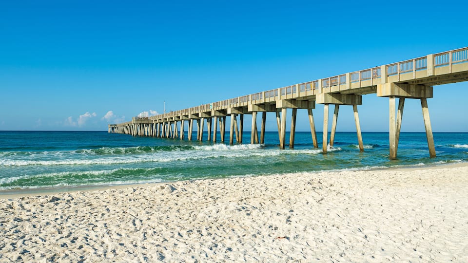 A long pier extending into the ocean with a sandy beach in the foreground.