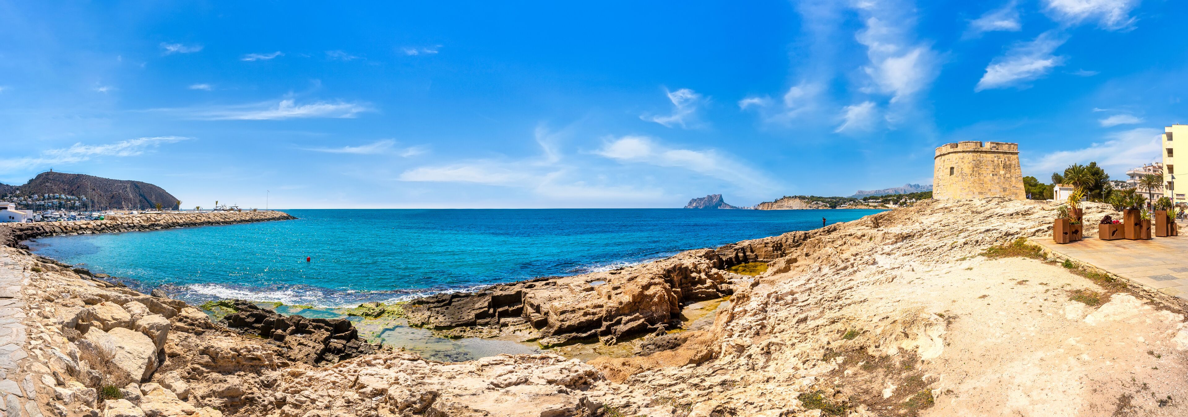 A coastal landscape with a rocky shoreline, a clear blue sea, and a historic tower.
