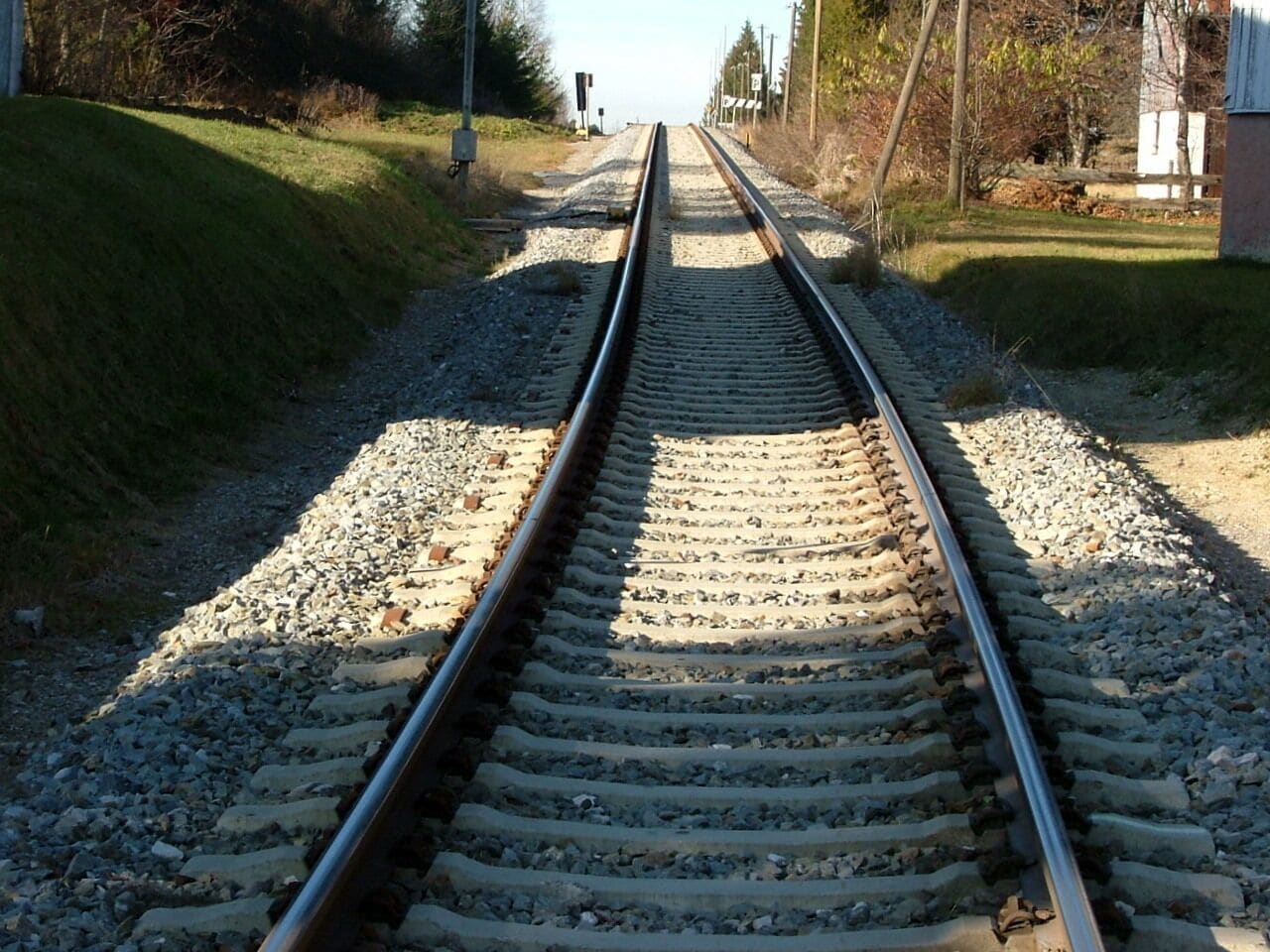 Railway tracks leading into the distance with gravel on either side and a grassy embankment on the left.