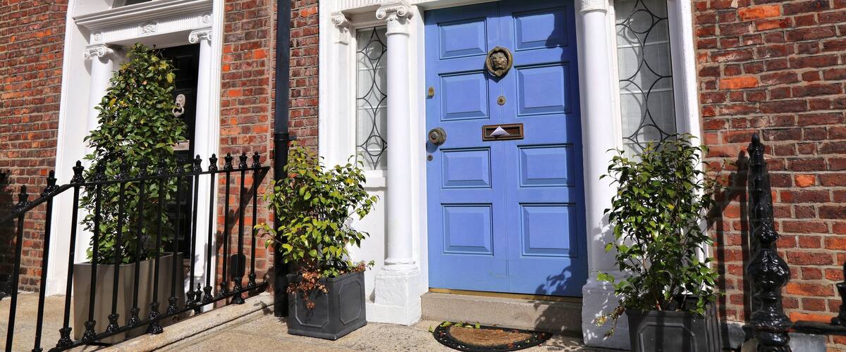 A red brick building with a blue door, white trim, and a black wrought iron fence.