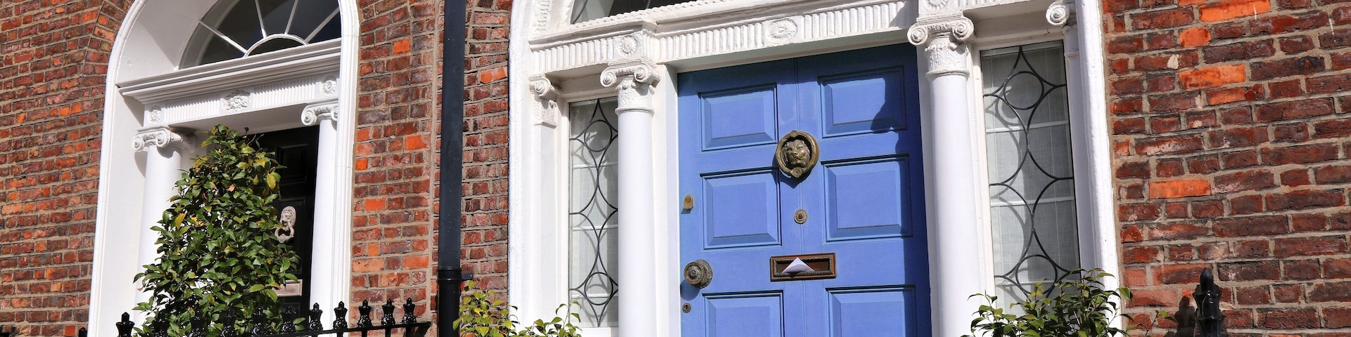 A red brick building with a blue door, white trim, and a black wrought iron fence.