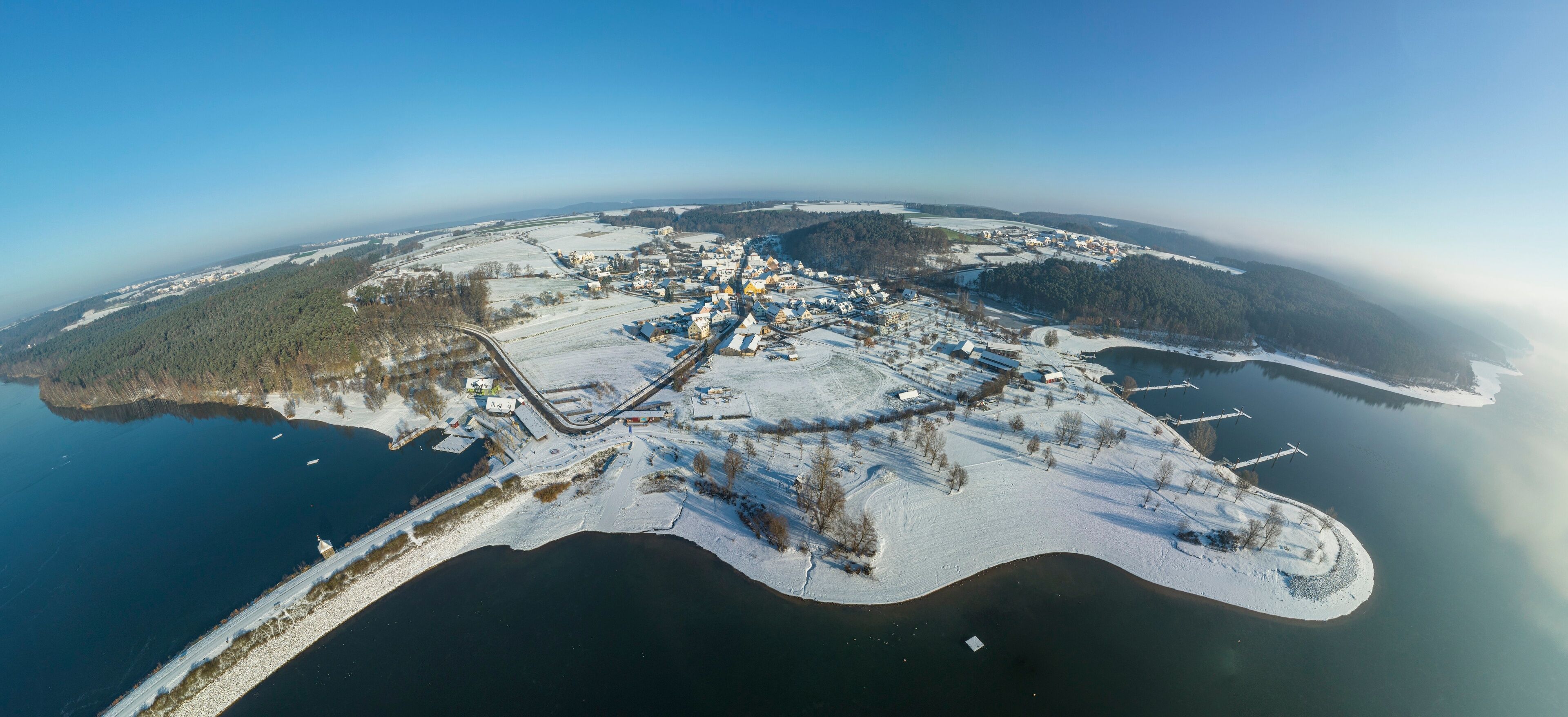 An aerial view of a snow-covered island with a small town, a railway line, and a lake.