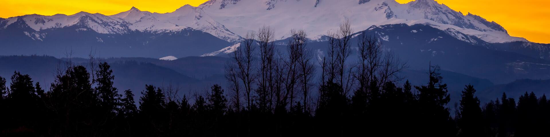 Orange and Yellow Sky at Sunrise in the Fraser Valley of British Columbia, Canada with Mount Baker, a dormant volcano in Washington State, on the horizon