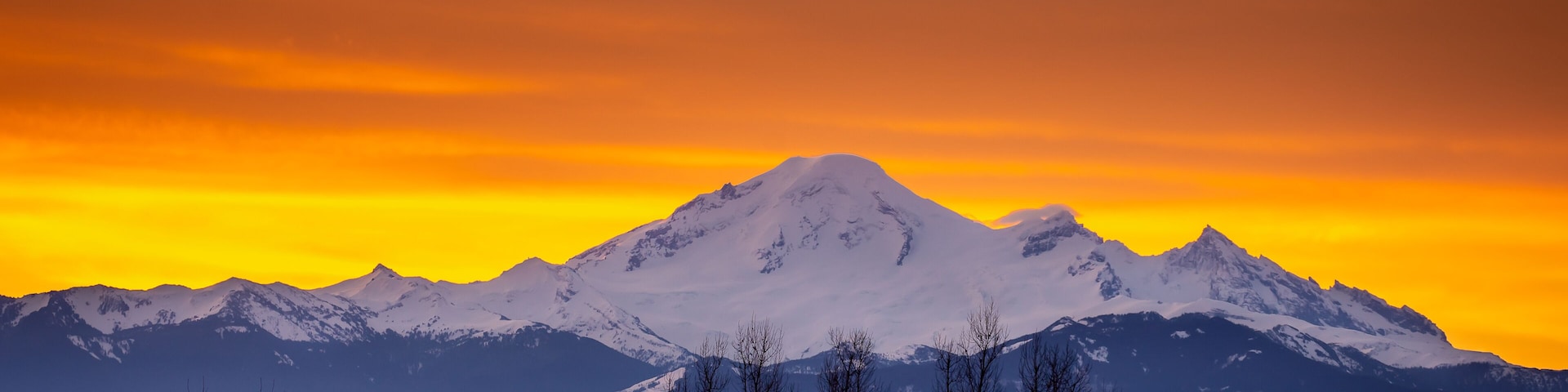 Orange and Yellow Sky at Sunrise in the Fraser Valley of British Columbia, Canada with Mount Baker, a dormant volcano in Washington State, on the horizon