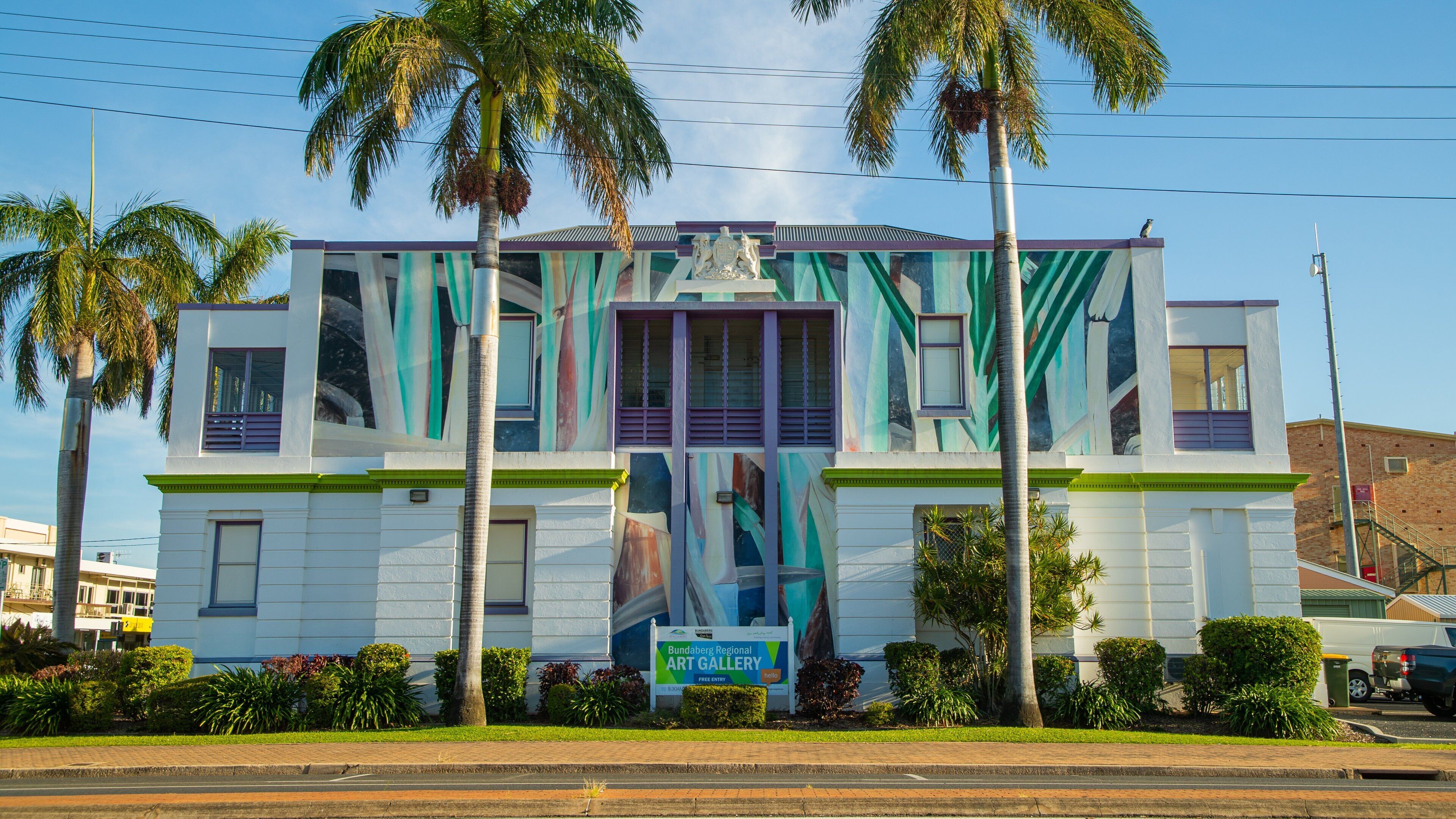 A building with a colorful mural, palm trees, and a sign for the Bundaberg Regional Art Gallery.