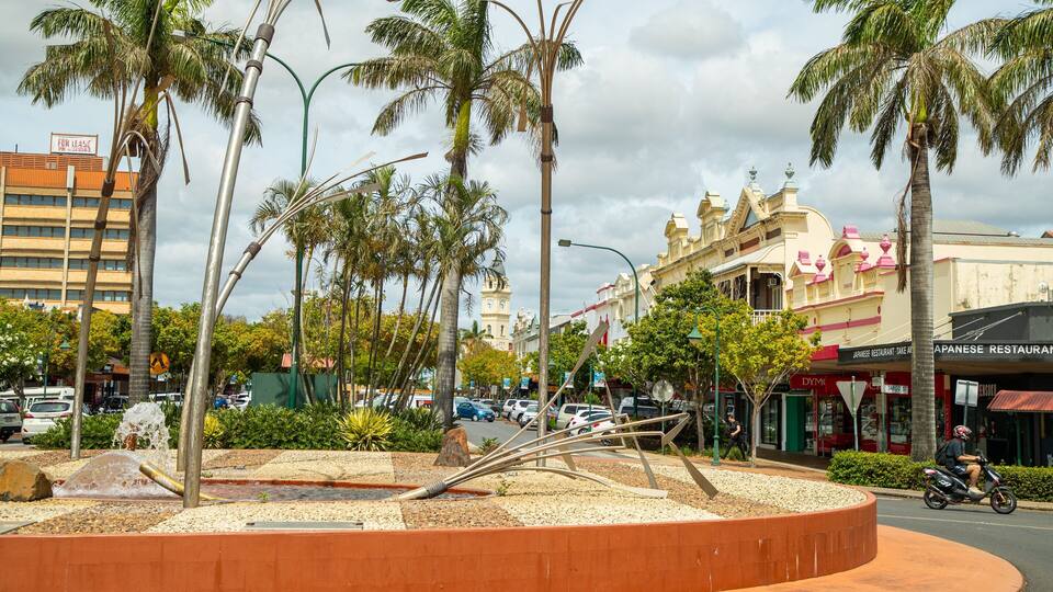 A street with palm trees, a fountain, and buildings with shops.