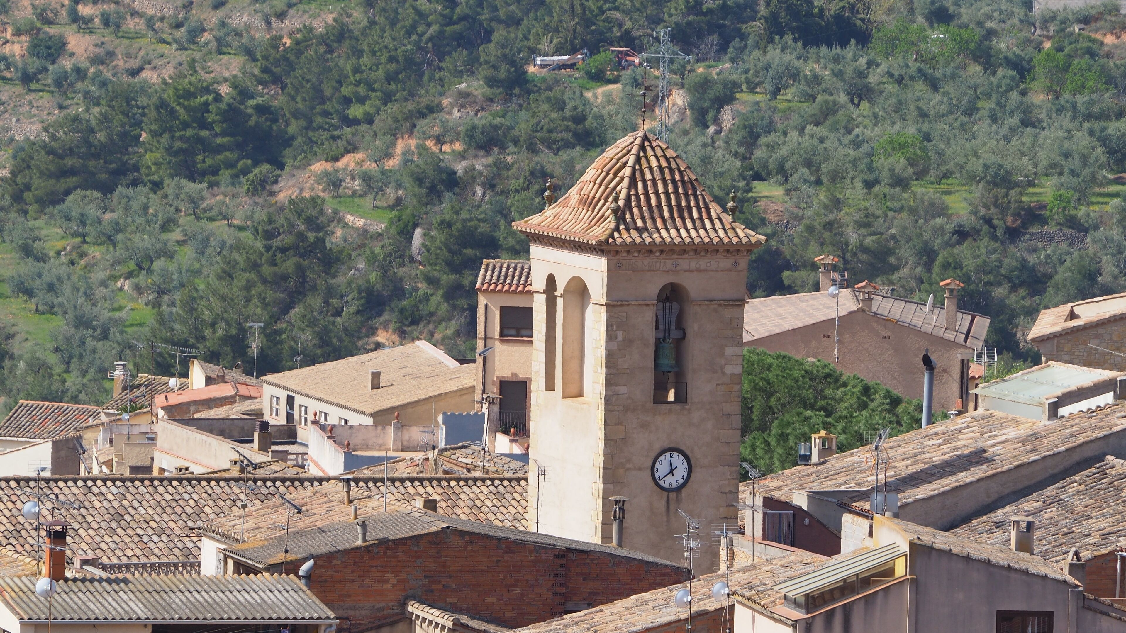 A tower with a clock, surrounded by traditional buildings with terracotta roofs.