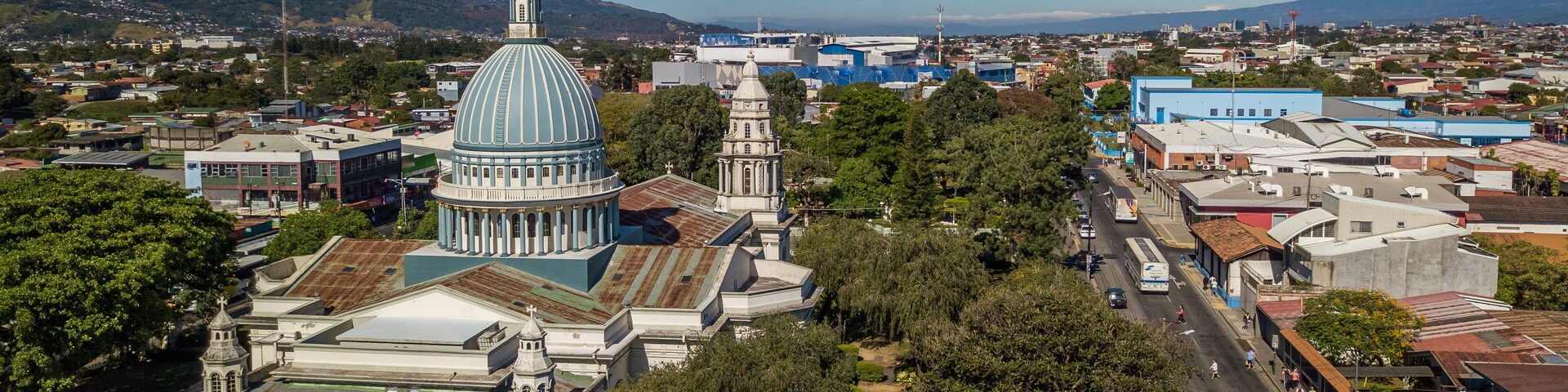 Paisagem urbana com uma cúpula imponente e um campanário, cercada por vegetação e edifícios.