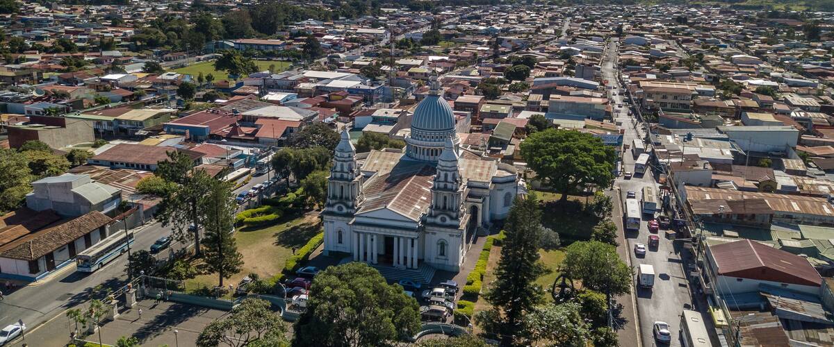 An aerial view of a city with a prominent cathedral, surrounded by residential areas and mountains in the background.