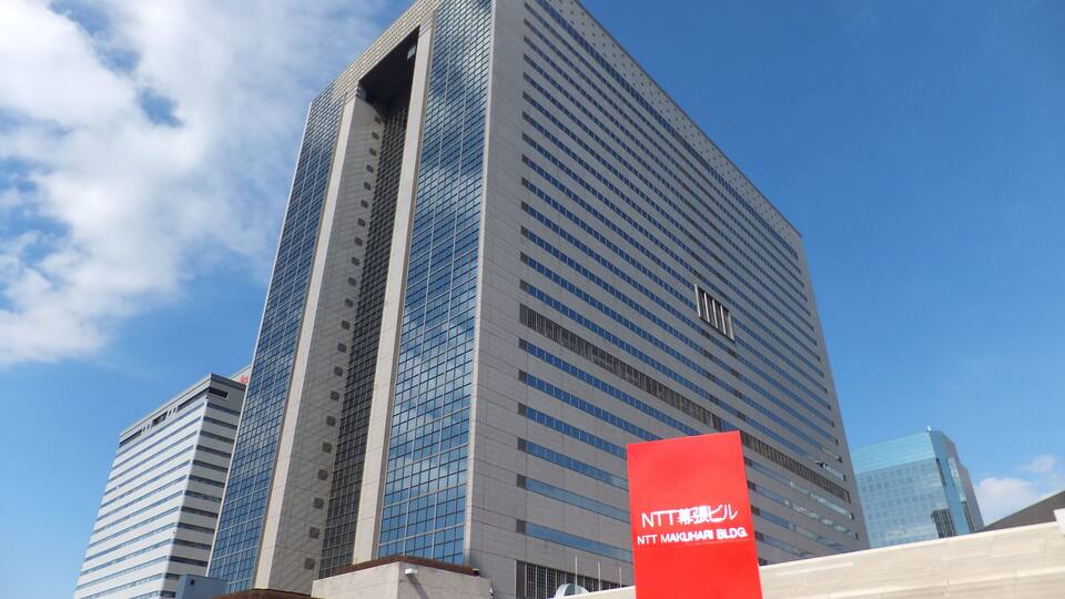 A tall modern building with reflective glass windows and a red sign in front.