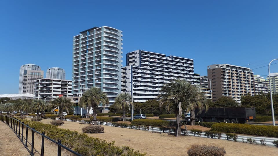 A cityscape with modern high-rise buildings, palm trees, and a well-maintained park area.