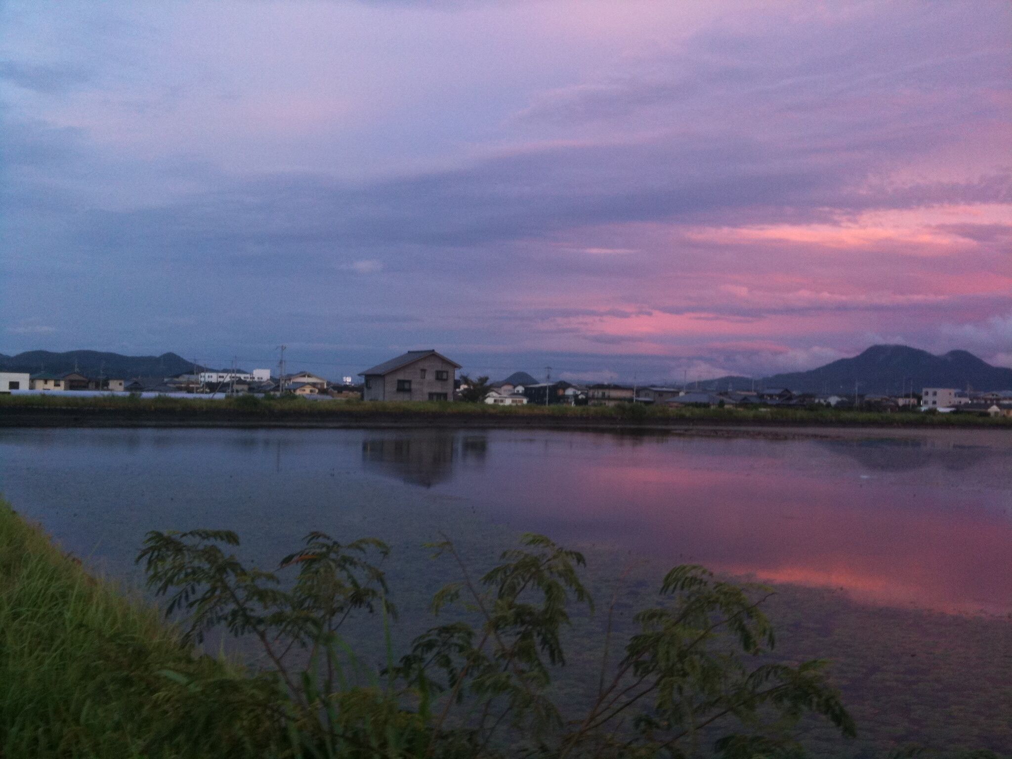 A calm lake with reflections of houses and mountains during twilight.