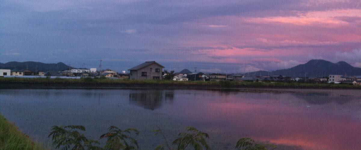 A calm lake with reflections of houses and mountains during twilight.