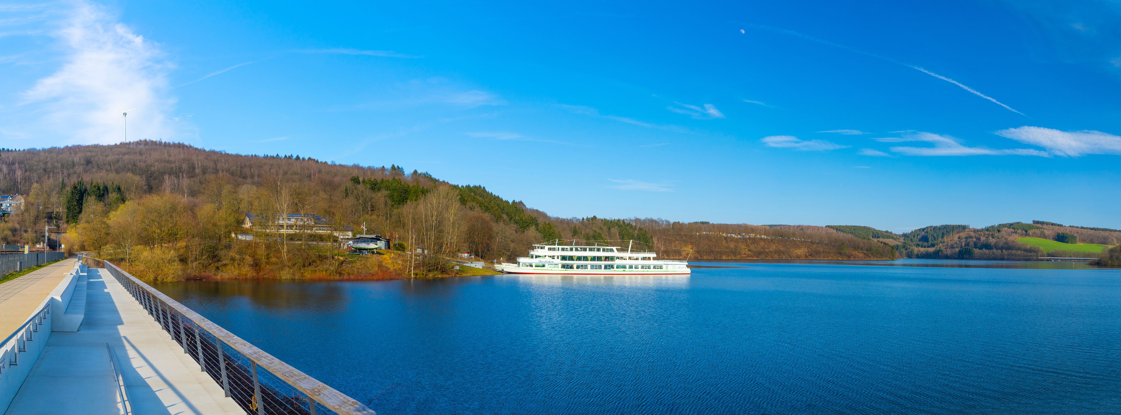 A river with a white boat, a bridge, and hills with trees.