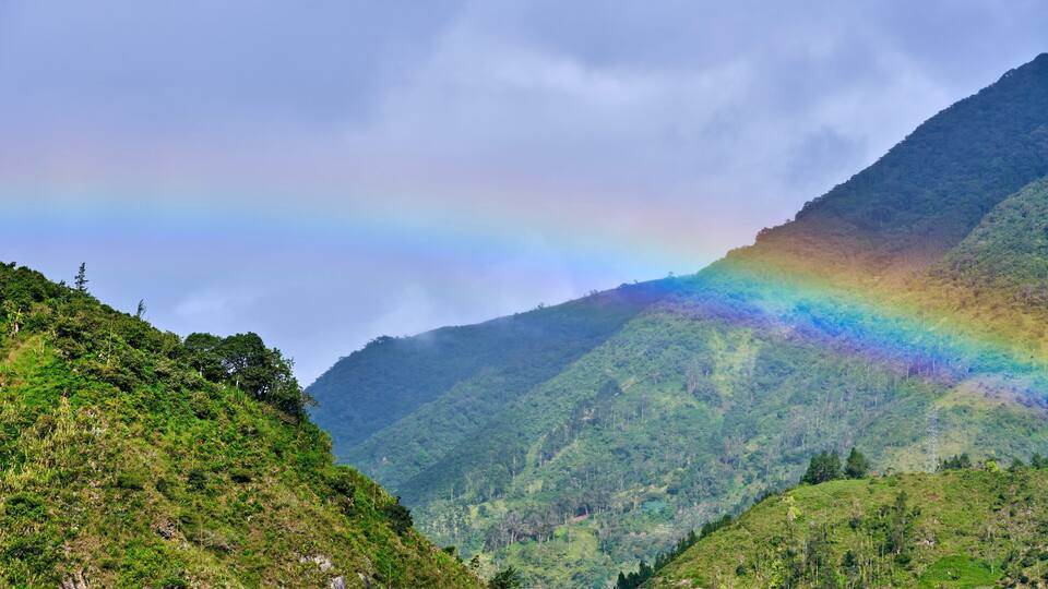 A lush green valley with a mountain range and a rainbow in the sky.