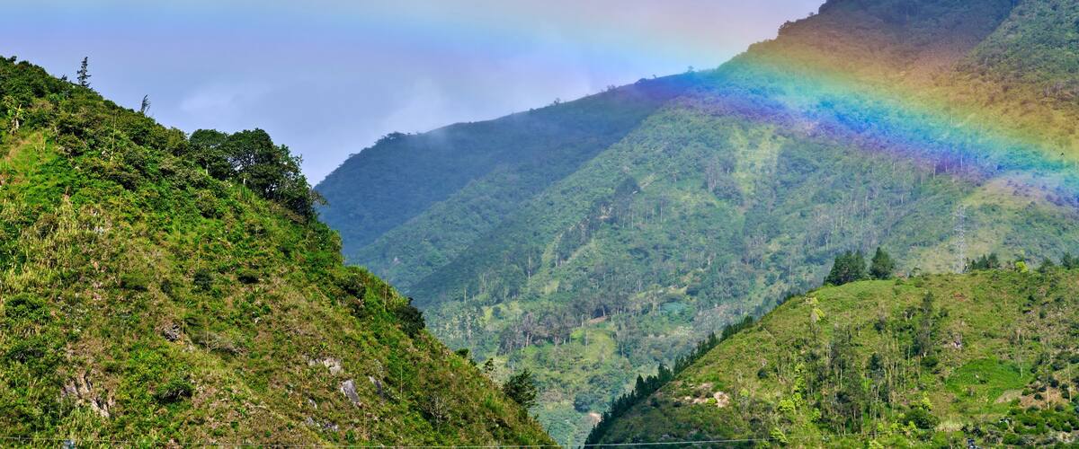 A lush green valley with a mountain range and a rainbow in the sky.