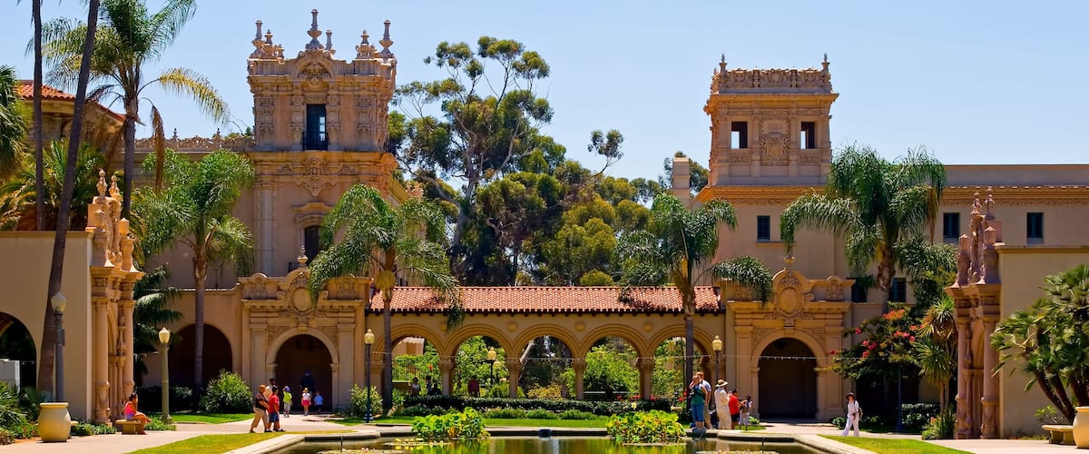 A historic building with ornate architecture, a central water feature with lily pads, and palm trees.