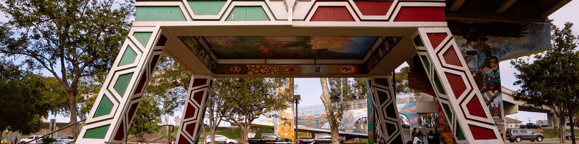 A colorful, geometric structure with stairs leading up to it, under a bridge.