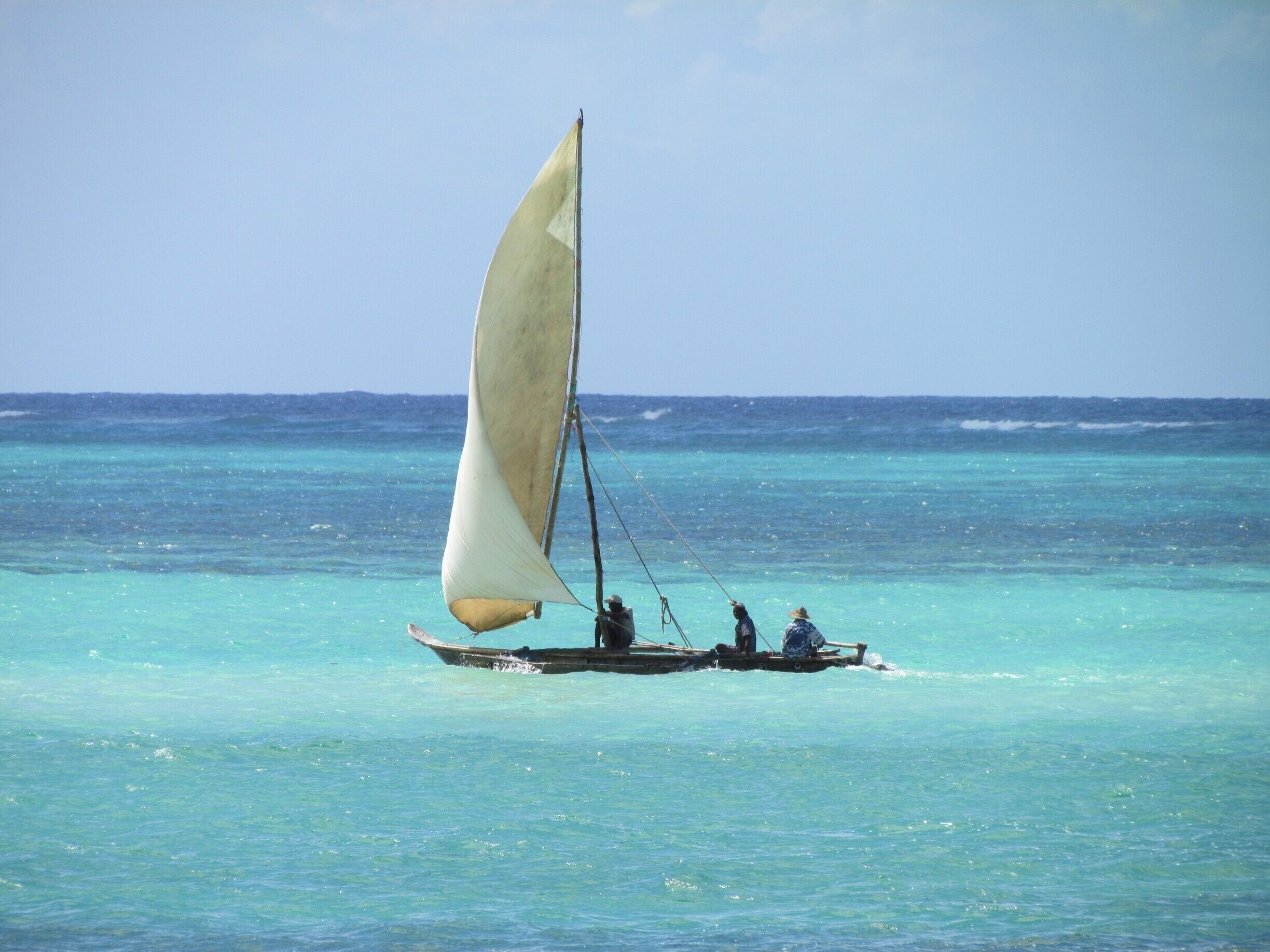 A traditional sailboat with a single sail on turquoise waters.