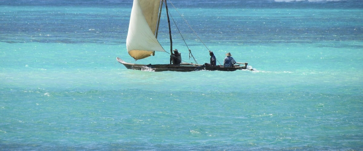 A traditional sailboat with a single sail on turquoise waters.