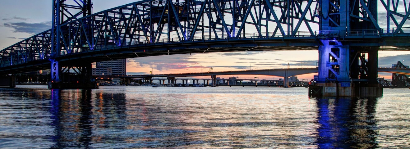 Un puente de acero con iluminación azul sobre aguas tranquilas, reflejando la estructura.