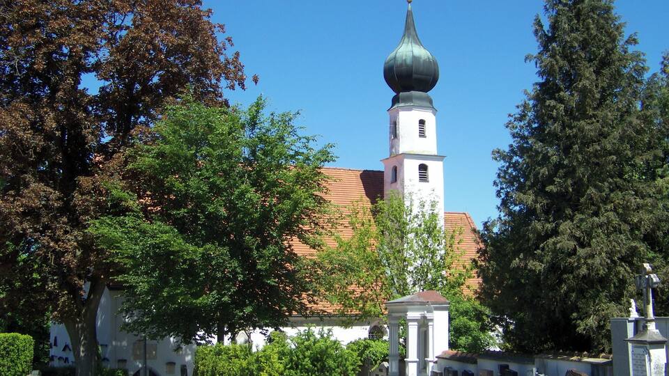 A cemetery with gravestones, a church with a bell tower, and surrounding trees.