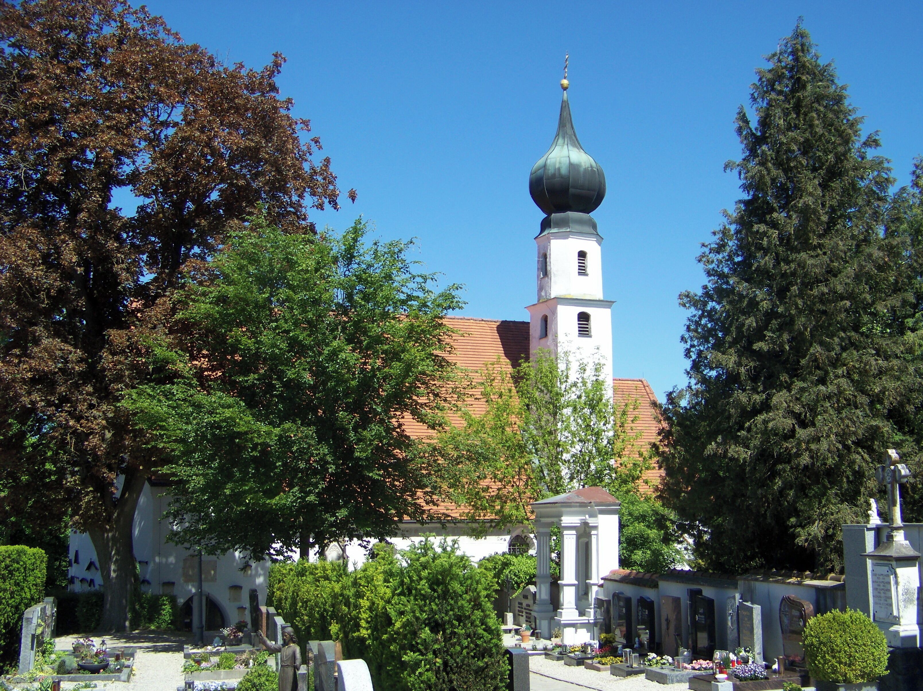 A cemetery with gravestones, a church with a bell tower, and surrounding trees.