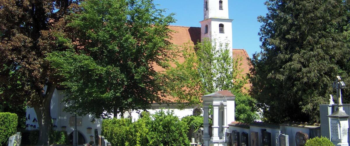 A cemetery with gravestones, a church with a bell tower, and surrounding trees.