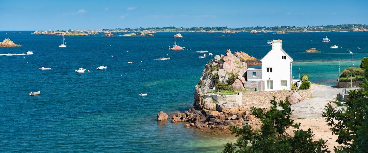 A coastal scene with a white building on a rocky outcrop, surrounded by clear blue waters and several boats.