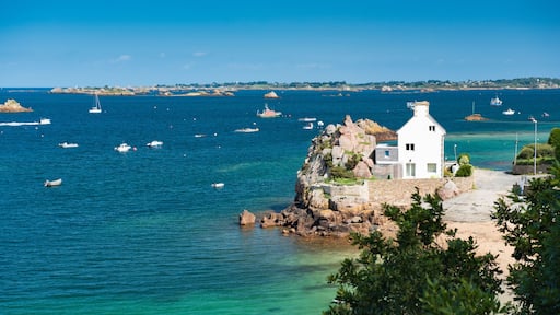 A coastal scene with a white building on a rocky outcrop, surrounded by clear blue waters and several boats.