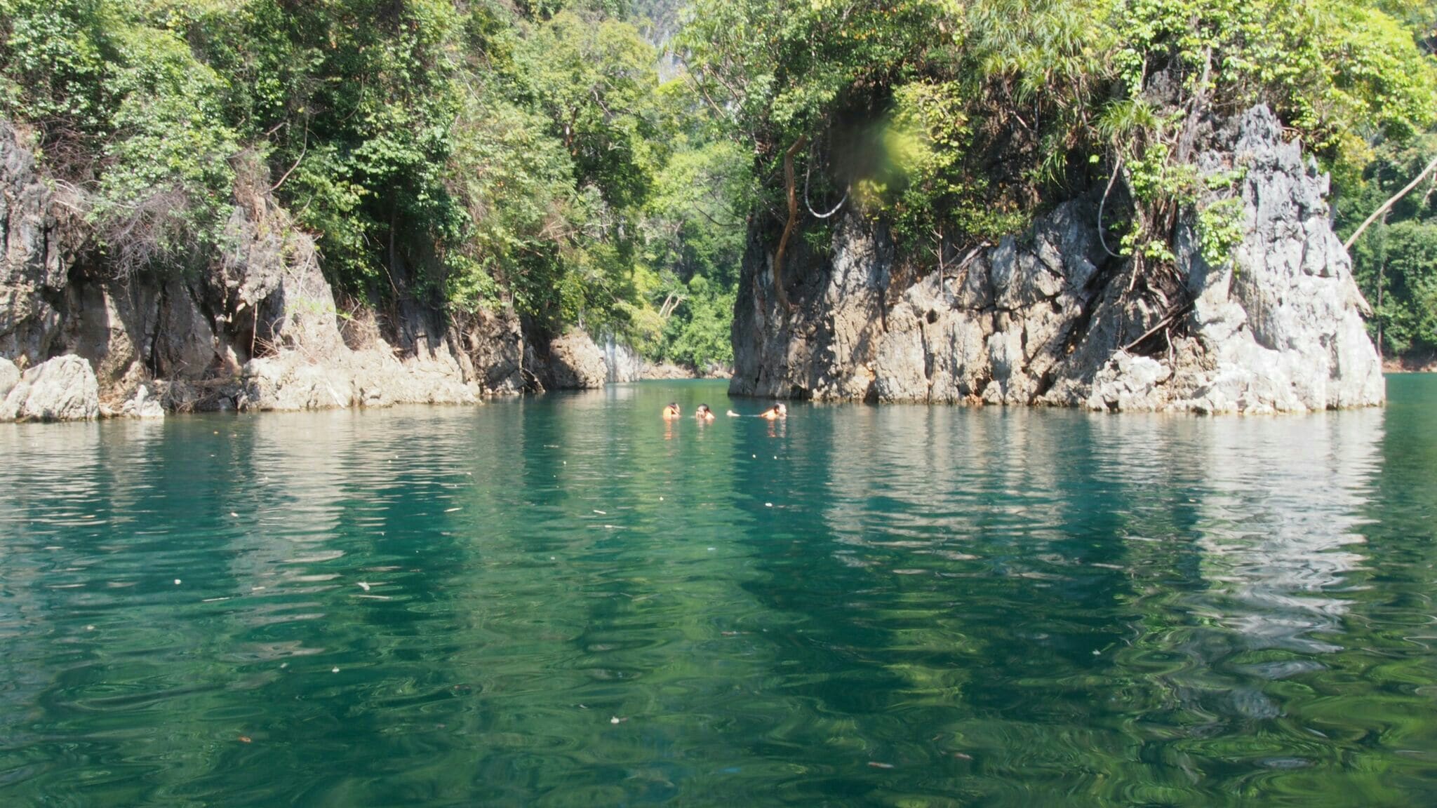 A clear turquoise lake surrounded by rocky cliffs and dense greenery.