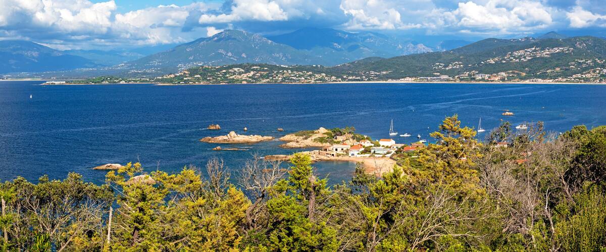 A coastal landscape with a clear view of the sea, rocky outcrops, and a distant mountain range.
