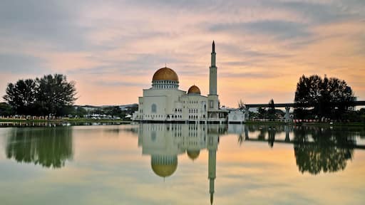 A mosque with a golden dome and a tall minaret, reflecting in a calm body of water.