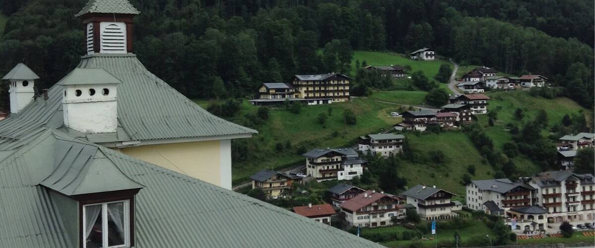 A mountain village with traditional houses, a church with a green roof, and a forested mountain backdrop.