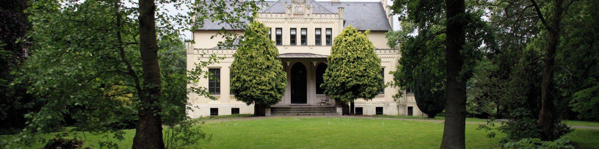 A stately building with a symmetrical facade, surrounded by lush greenery and tall trees.