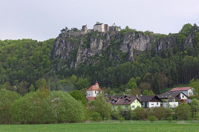 A castle on a cliff, surrounded by houses and greenery.