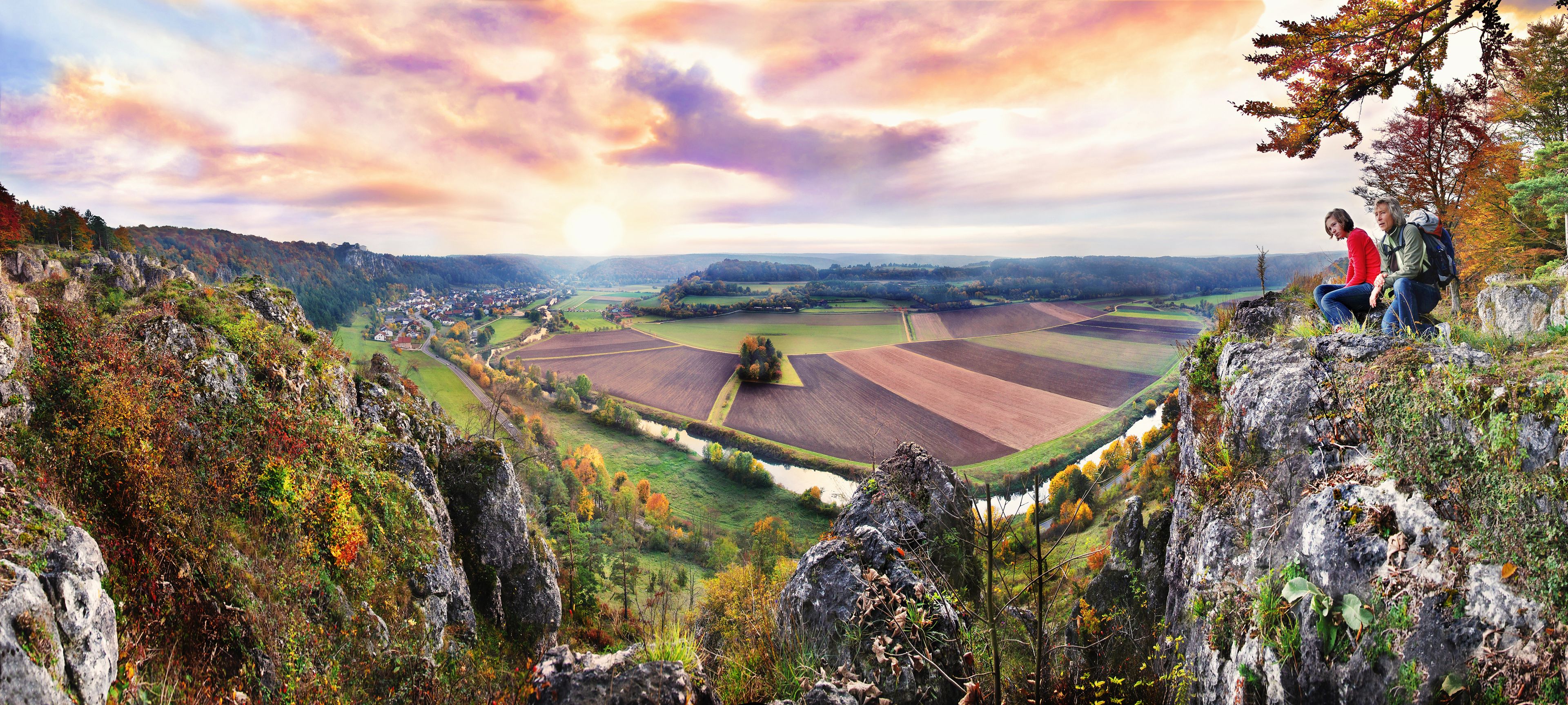A panoramic view of a valley with fields, a river, and a town in the distance.