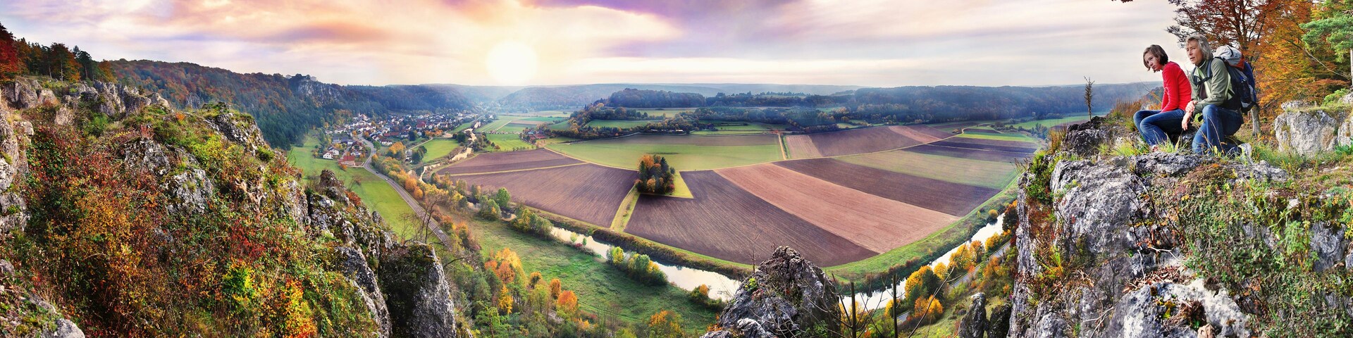 Una vista panorámica de un valle con campos, un río y un pueblo a lo lejos.