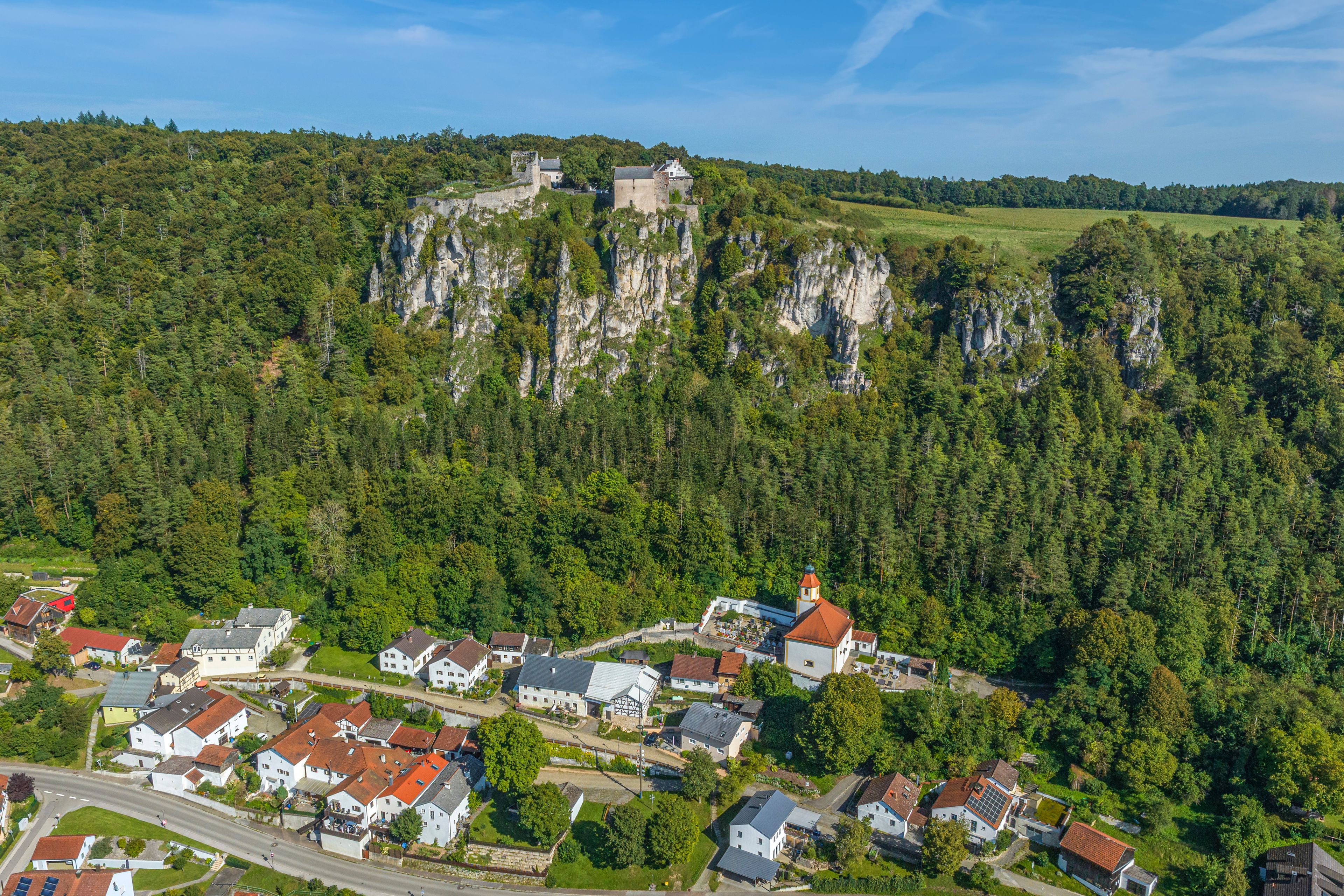 A village nestled in a valley with a prominent castle on a rocky hill in the background.