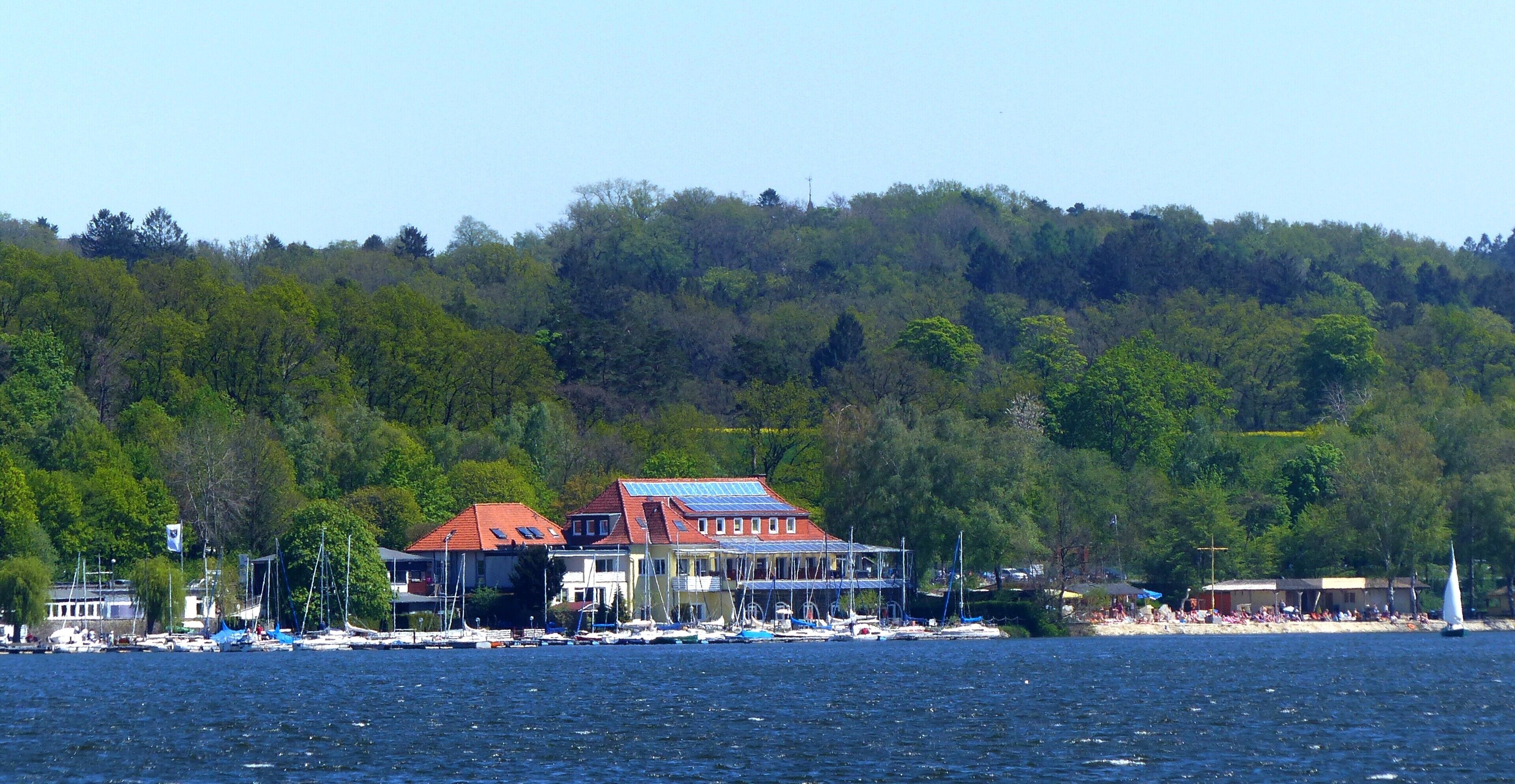 A coastal town with houses, boats, and a forested hill in the background.