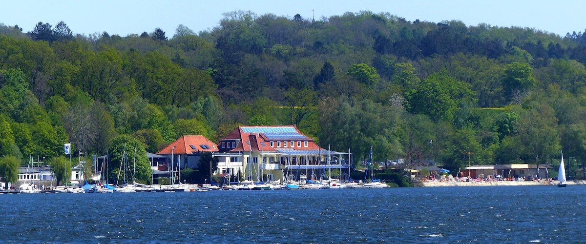 A coastal town with houses, boats, and a forested hill in the background.