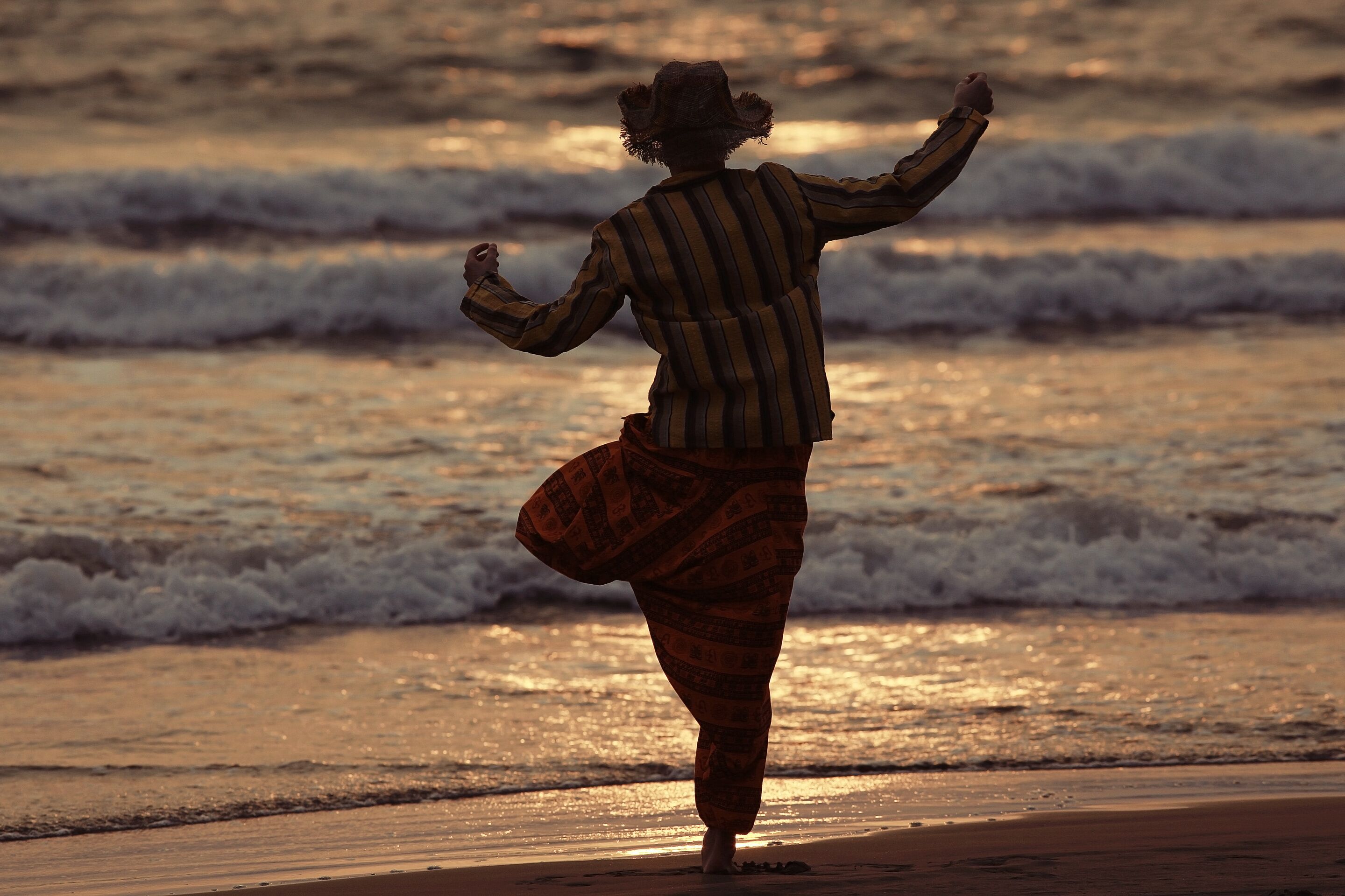 A person walking on a beach with waves in the background.