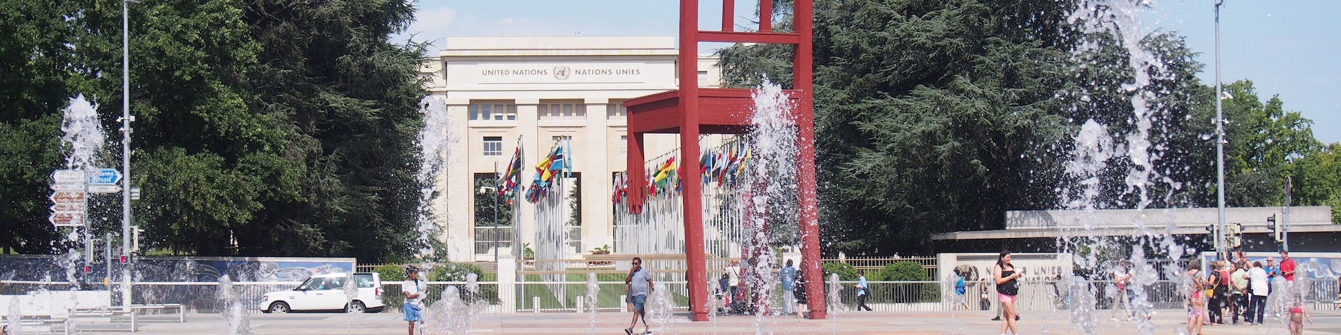 Una plaza pública con una gran escultura roja, fuentes y un edificio con banderas.