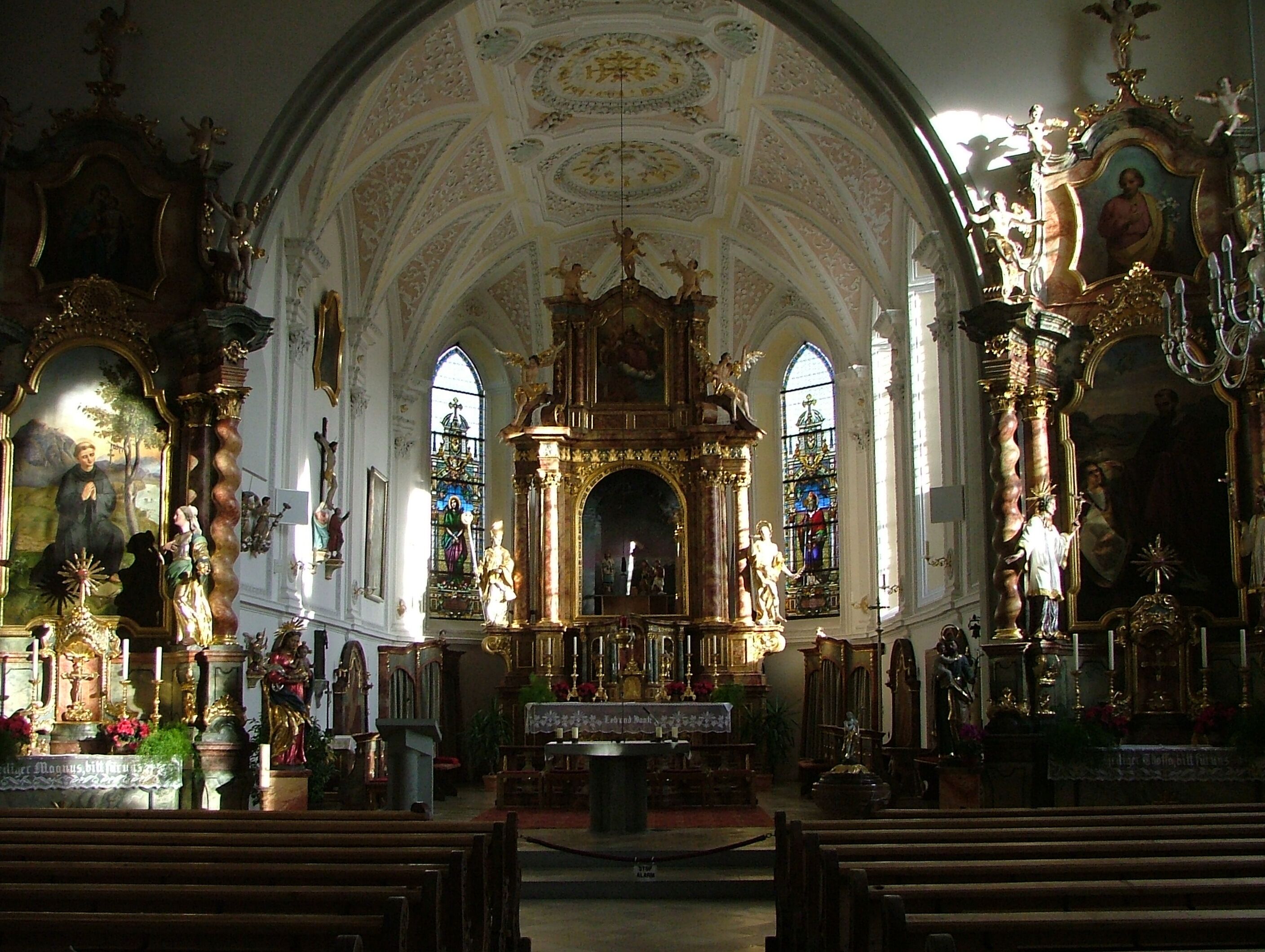 An ornate church interior with a high vaulted ceiling, stained glass windows, and religious statues.