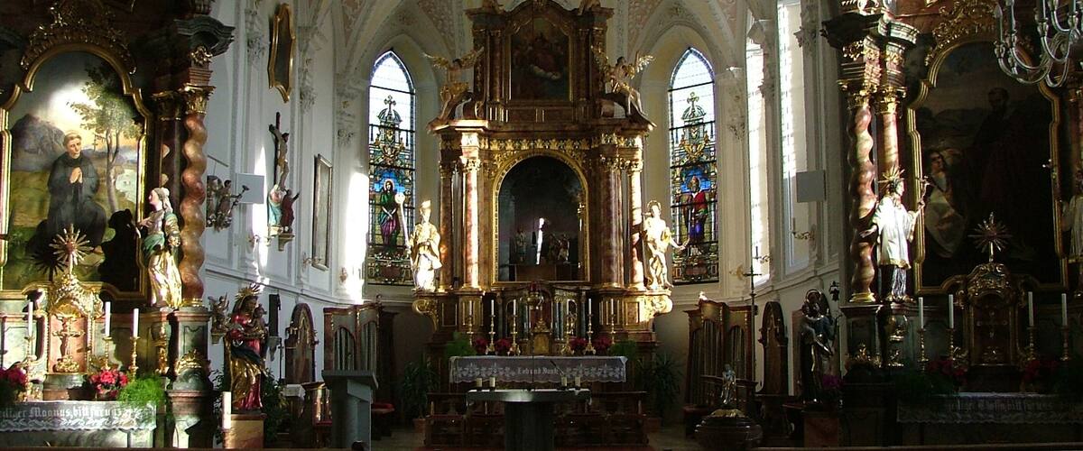 An ornate church interior with a high vaulted ceiling, stained glass windows, and religious statues.