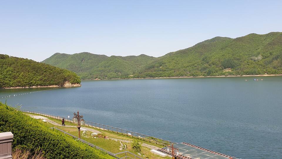 A calm lake surrounded by lush green hills and a walking path along the water's edge.